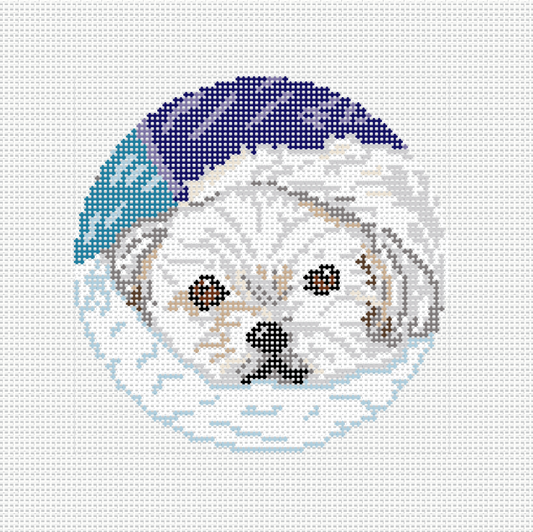 Needlepoint canvas of a white Maltese wearing a navy blue winter hat with a snowflake border, circular ornament format